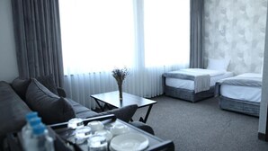 A hotel room with a sofa, two single beds, a small table with a vase, and a view through sheer curtains. - BMG Hotel  (Goris)