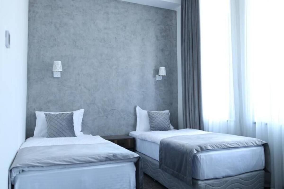 Habitación de hotel con dos camas, paredes grises y una ventana con cortinas.
