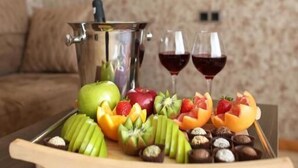 A tray with fruits and chocolates on a wooden table, a metal container, and two glasses of red wine. - BMG Hotel  (Goris)