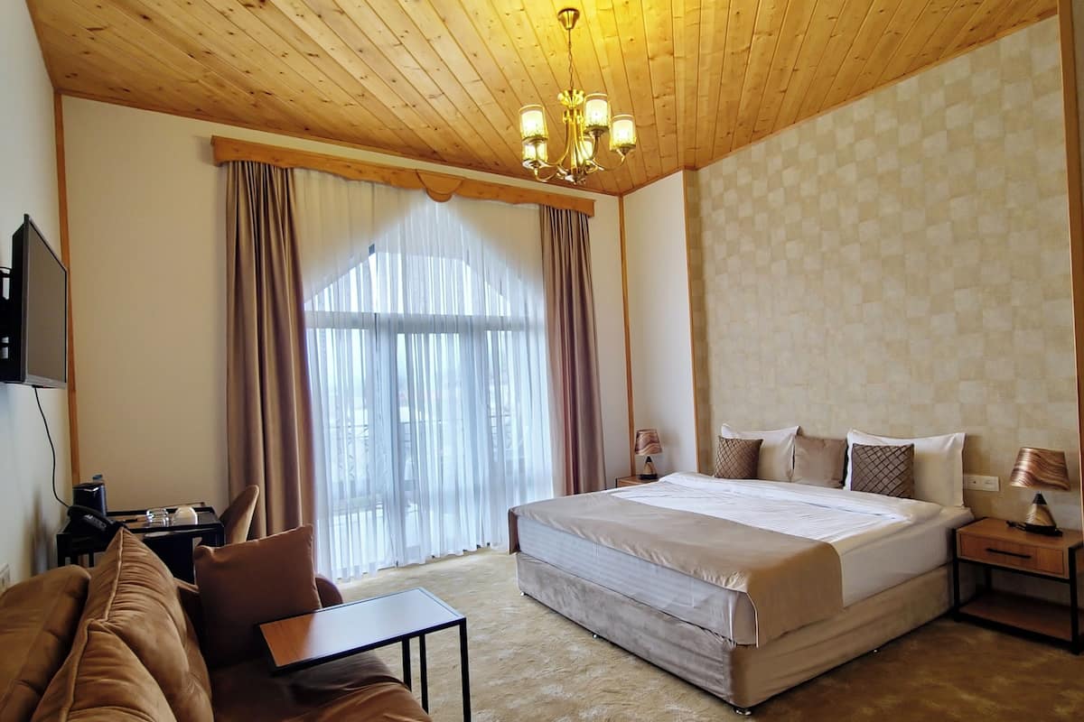Un dormitorio con techo de madera, una cama grande, un sofá, un escritorio y un ventanal con cortinas.