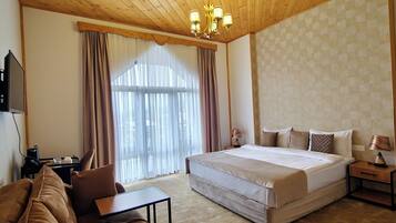 A bedroom with a wooden ceiling, a large bed, a sofa, a desk, and a window with curtains.