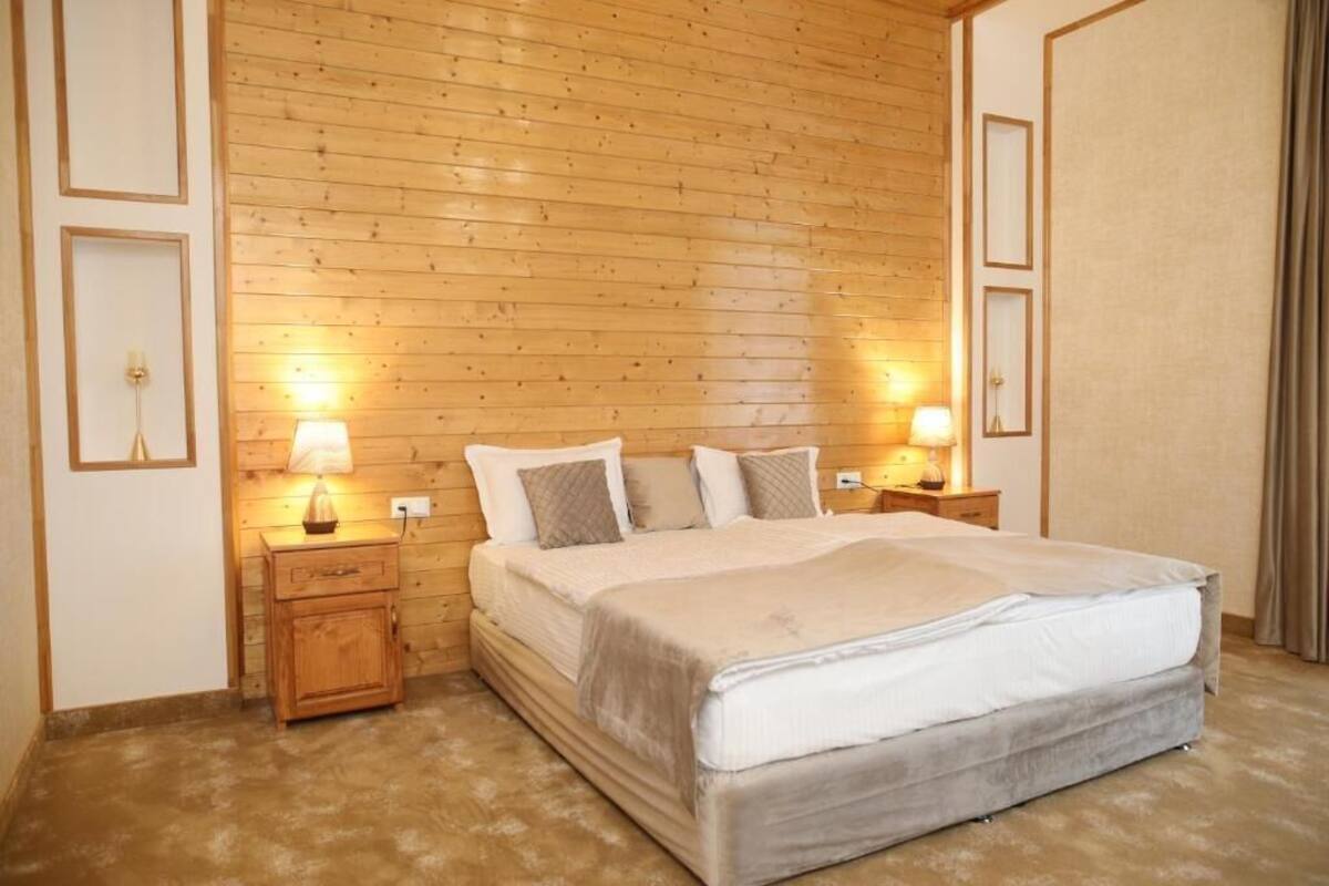 Un dormitorio con pared de paneles de madera, una cama con colchón gris, dos mesitas de noche con lámparas y un armario de madera.