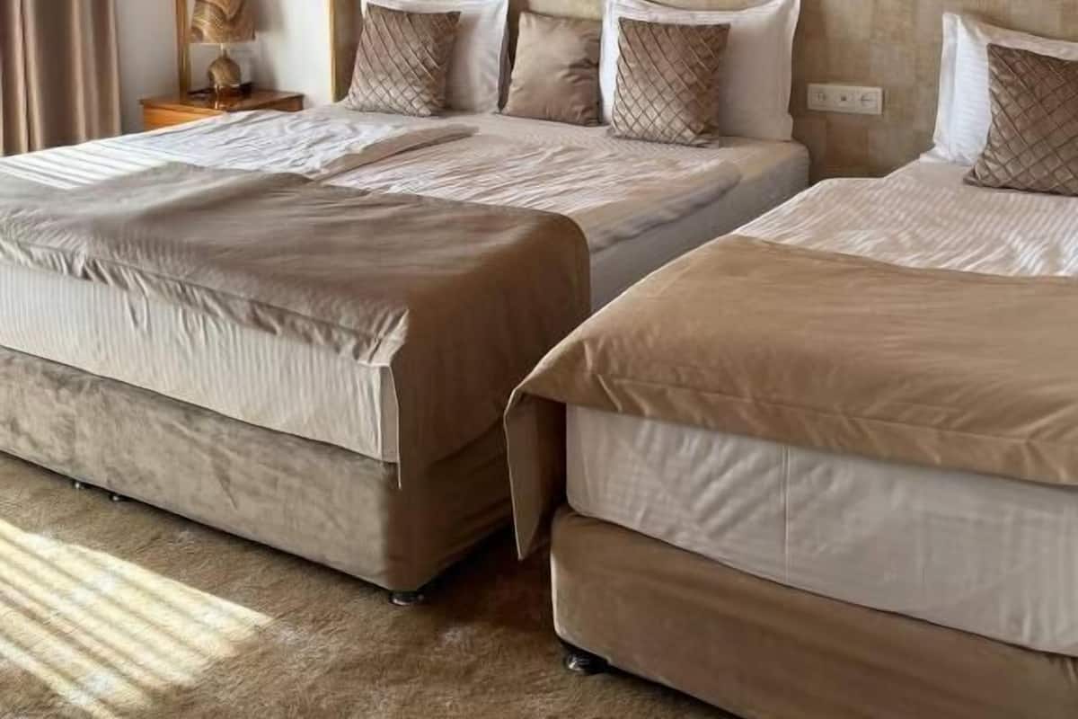 Habitación de hotel con dos camas, un muro a cuadros, techo de madera y una mesita de noche con lámpara.