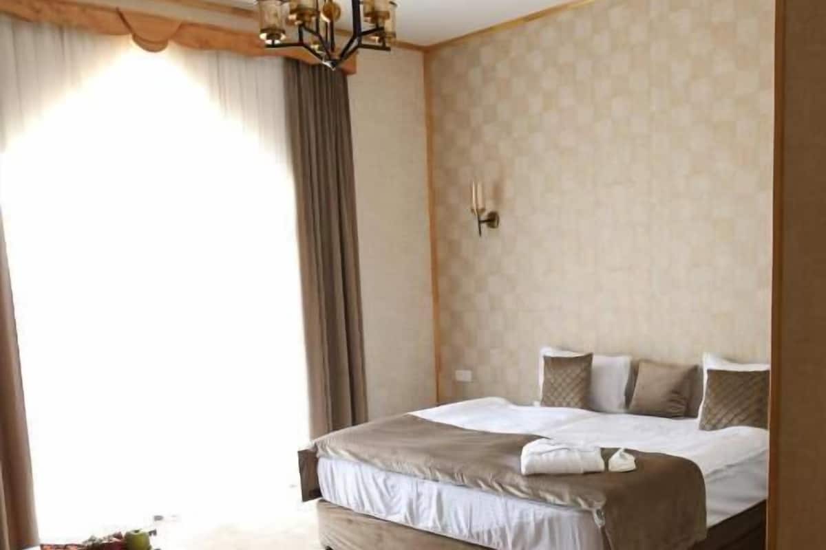Habitación de hotel con una cama grande, un candelabro, una mesita con fruta y vistas al exterior.