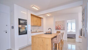A modern kitchen with built-in appliances, a wooden island, and a dining area with bar stools. - Ray Holiday Apartment (Okrug Gornji)
