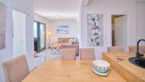 A modern living room with a sofa, a dining table, and a kitchen area with a sink. - Ray Holiday Apartment (Okrug Gornji)