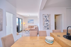 A modern living room with a sofa, a dining table, and a kitchen area with a sink. - Ray Holiday Apartment (Okrug Gornji)