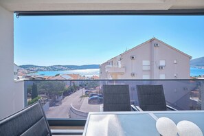 A balcony with a view of a coastal town, a table with chairs, and a glass partition. - Ray Holiday Apartment (Okrug Gornji)