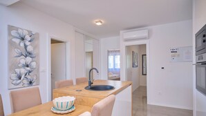A modern kitchen with a wooden island, white cabinetry, a built-in sink, and a dining area with chairs. - Ray Holiday Apartment (Okrug Gornji)