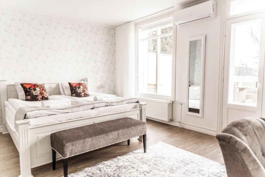 Une chambre à coucher avec un lit, un banc, de grandes fenêtres et un radiateur.