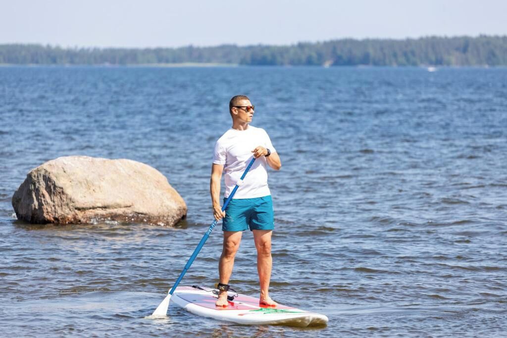 A person standing on a paddleboard in a body of water with a large rock nearby.