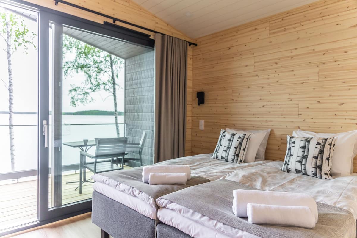 Un dormitorio con cama, almohadas, una mesita de noche, una ventana y vistas al exterior.