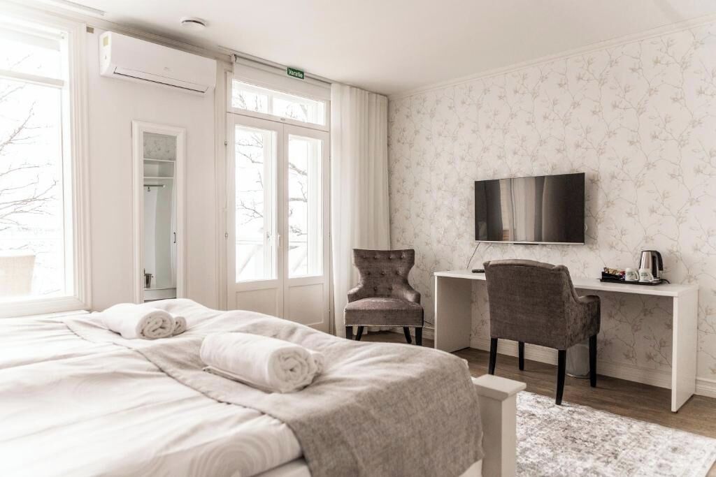 A hotel room with a bed, a desk, a chair, a TV, and a window.