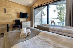 A modern bedroom with two beds, a TV, and a balcony with a view of the water. - Radalla Resort (Iitti)