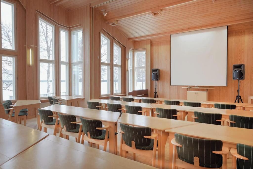 Une salle de conférence aux murs en bois, dotée de grandes fenêtres et d’un écran de projection blanc.