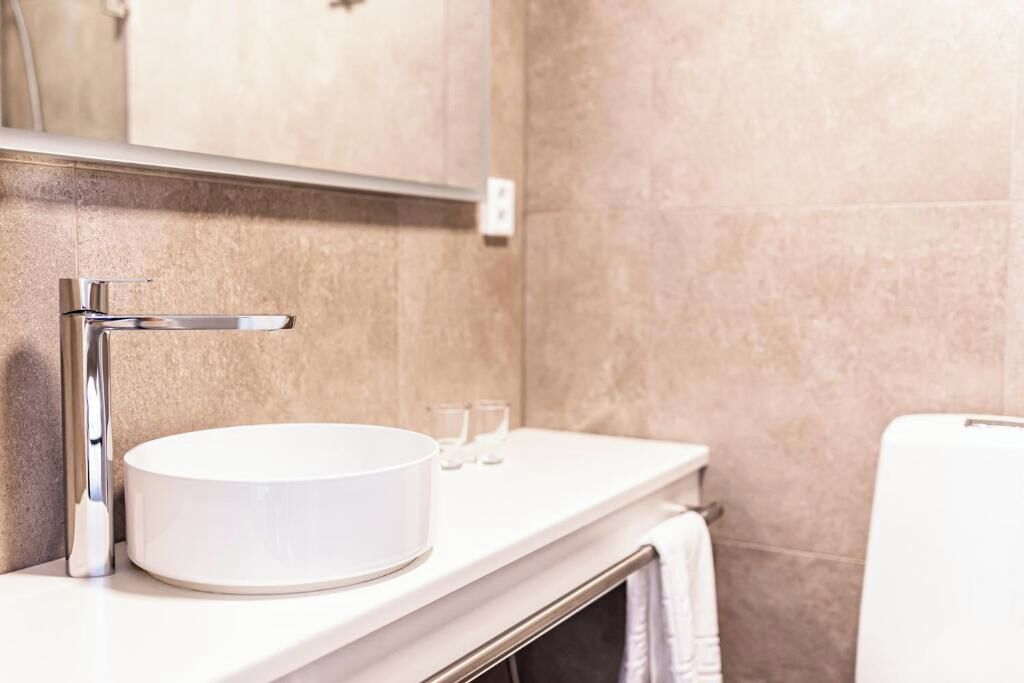 A bathroom with a round sink, a chrome faucet, a mirror, and a towel rack.