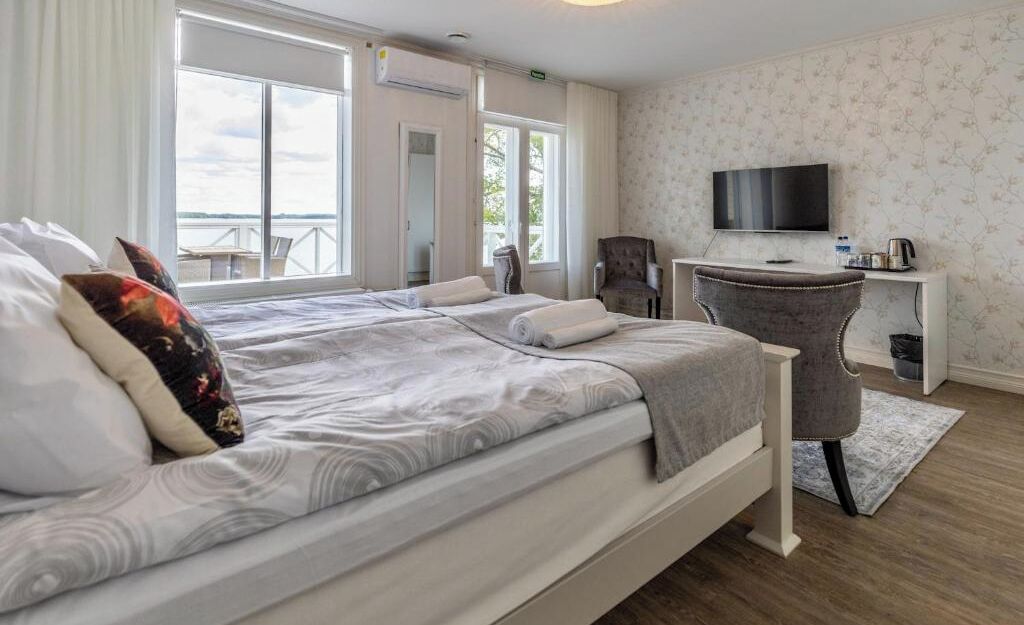 A hotel room with a bed, a desk, a chair, a TV, and a view of the outdoors.