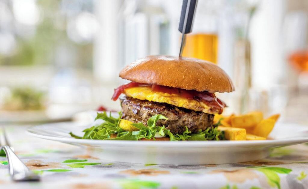 A burger with a knife on a plate, accompanied by fries and lettuce.