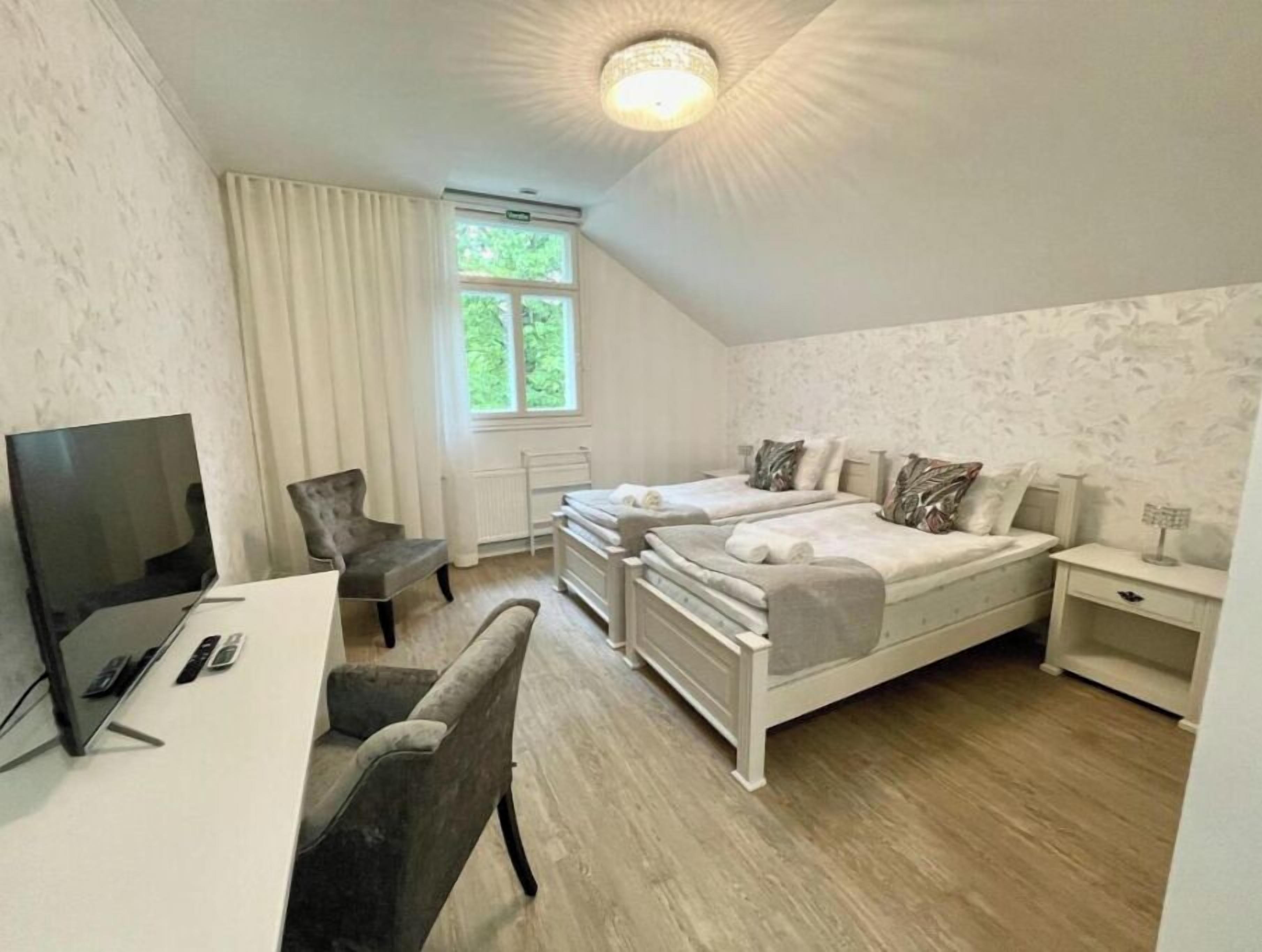 A bedroom with a bed, a desk, a chair, a TV, and a window.