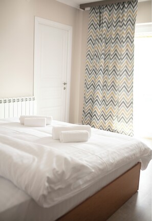 A neatly made bed with white linens and two rolled towels, a white door, and a chevron-patterned curtain. - RestArt Boutique Hotel (Dilijan)