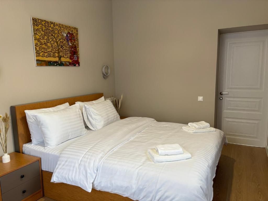 A neatly made bed with white linens, a wooden headboard, and a wall-mounted artwork.