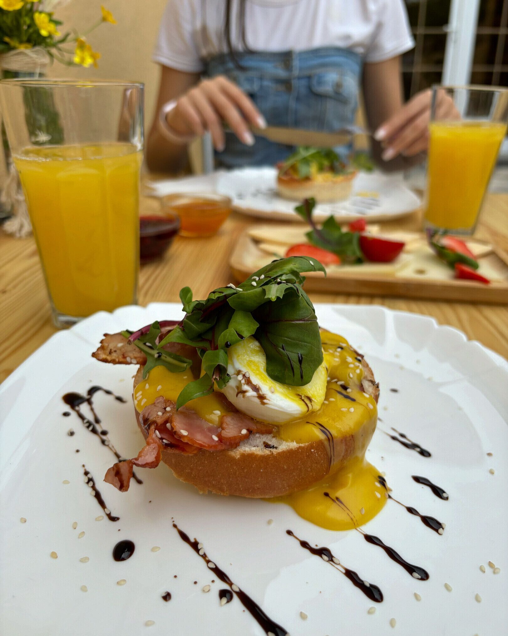 A breakfast plate with an egg, greens, and bacon on toast, accompanied by a glass of orange juice and a cup of tea.