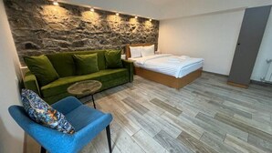 A bedroom with a stone wall, a bed, a green sofa, and a blue chair. - RestArt Boutique Hotel (Dilijan)