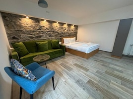 Un dormitorio con pared de piedra, una cama, un sofá verde y un sillón azul.