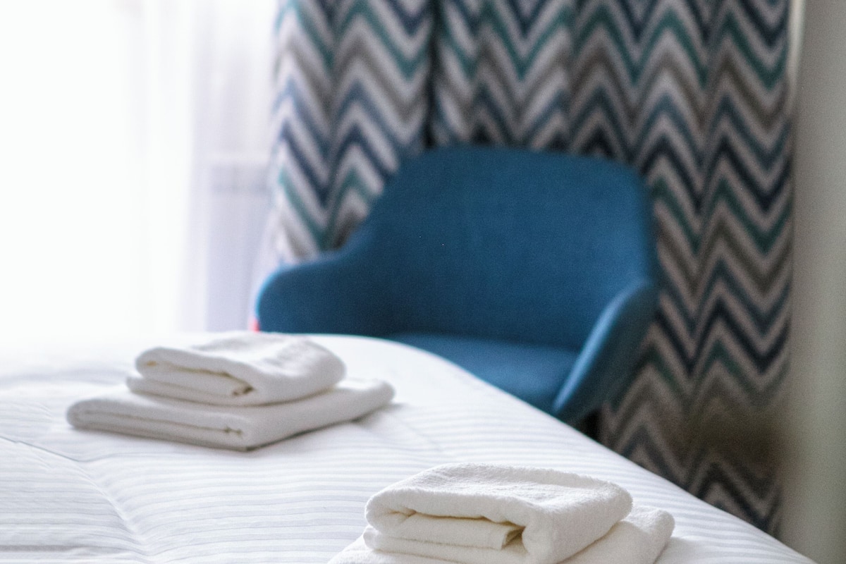 Une chambre d’hôtel avec un lit, une chaise bleue et un rideau à motifs.