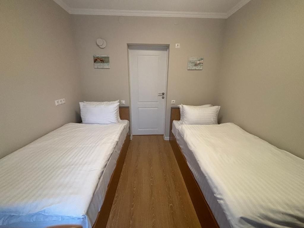 A room with two single beds, a wooden floor, a white door, and small wall decorations.