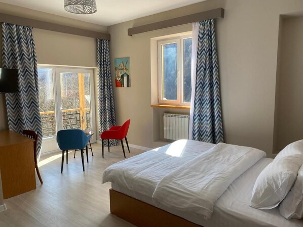 A bedroom with a bed, a desk, two chairs, a window with curtains, and a radiator. - RestArt Boutique Hotel (Dilijan)
