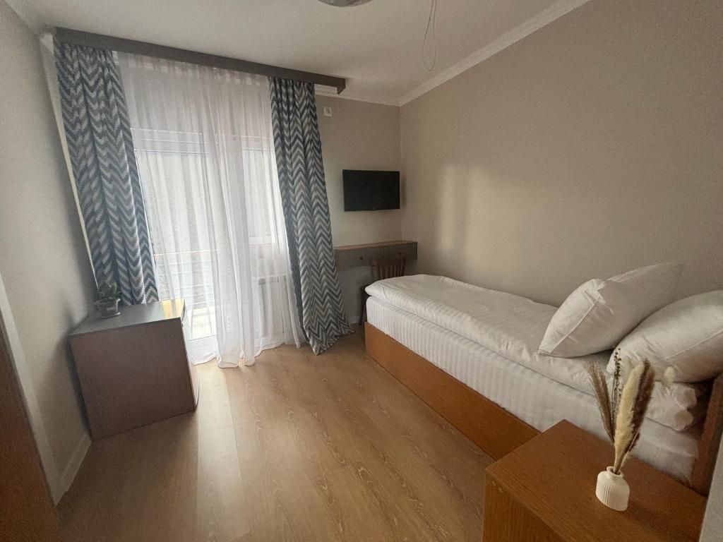 Een slaapkamer met een bed, een nachtkastje, een aan de muur bevestigde televisie en een raam met gordijnen.