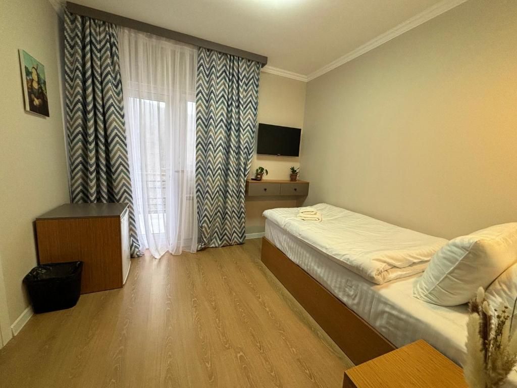 Een kleine, netjes ingerichte kamer met een bed, een bureau en een televisie aan de muur.