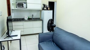 Een gezellig compact verblijf met een kitchenette, een bank, een klein tafeltje met een laptop en een ventilator.