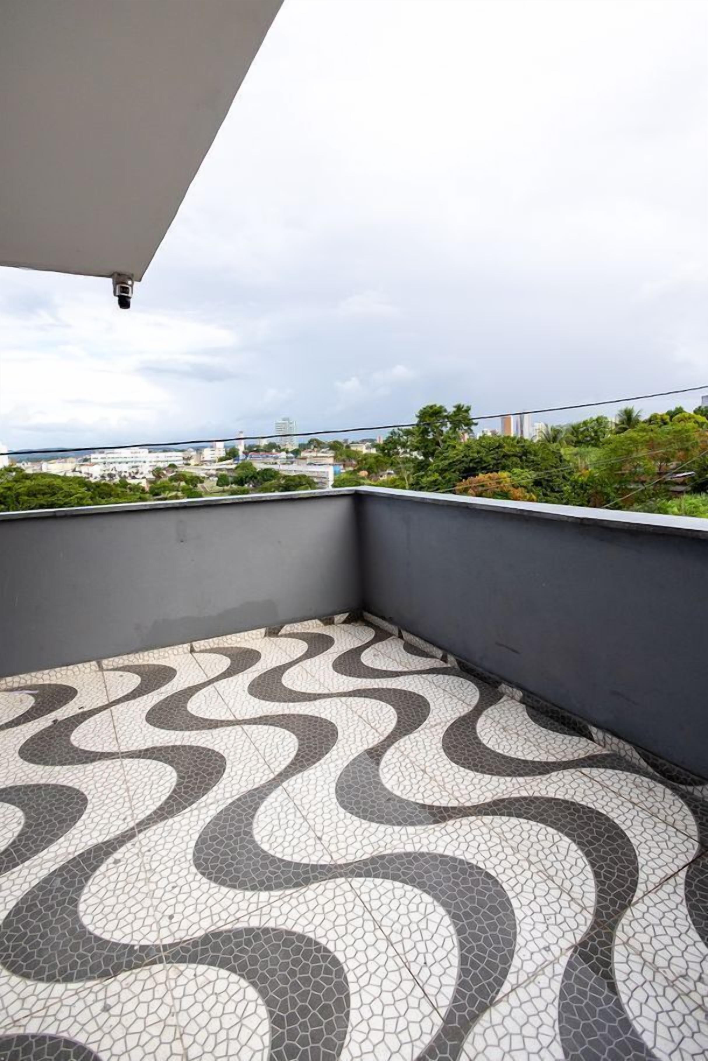 Un balcón con baldosas y un diseño curvo, una pared gris y una vista de un paisaje urbano al fondo.