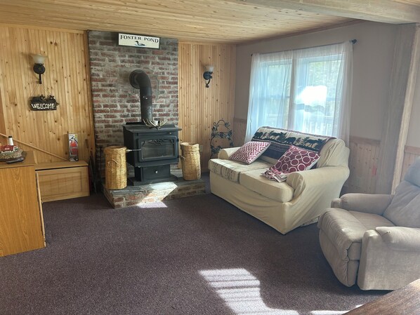 A cozy room with a fireplace, a sofa, a wooden cabinet, and a sign reading 'Foster Pond'.
