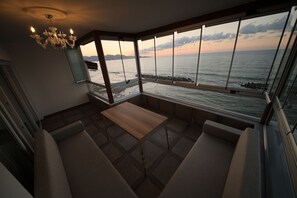 Une chambre moderne dotée d’une grande fenêtre donnant sur la mer, d’une table en bois et d’un lustre.