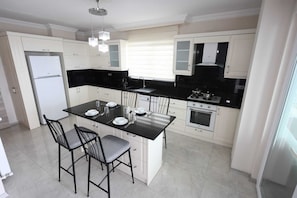 A modern kitchen with white cabinetry, a black countertop island, and a dining area with two chairs.