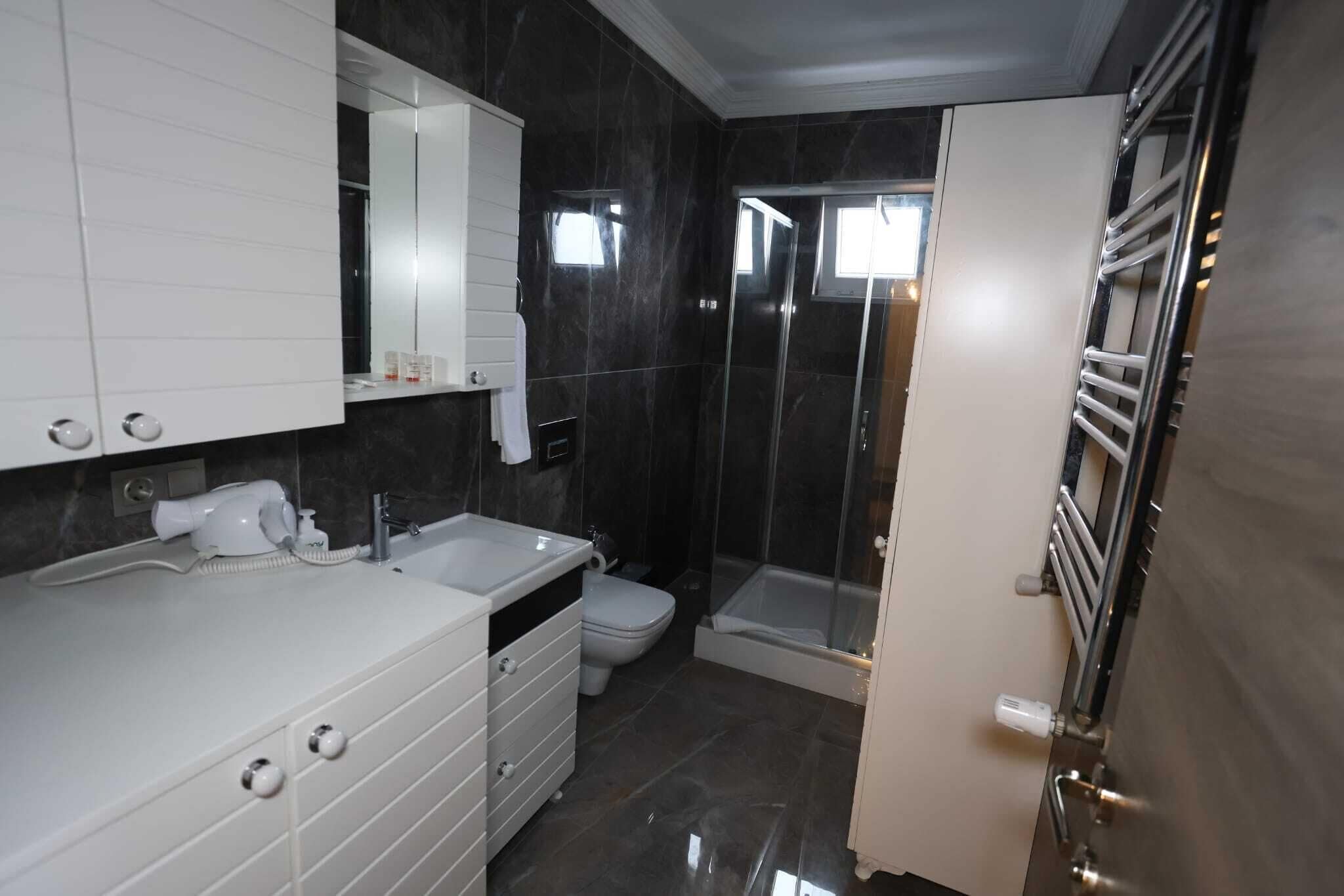 Un baño moderno con tocador blanco, inodoro, cabina de ducha y perchero.