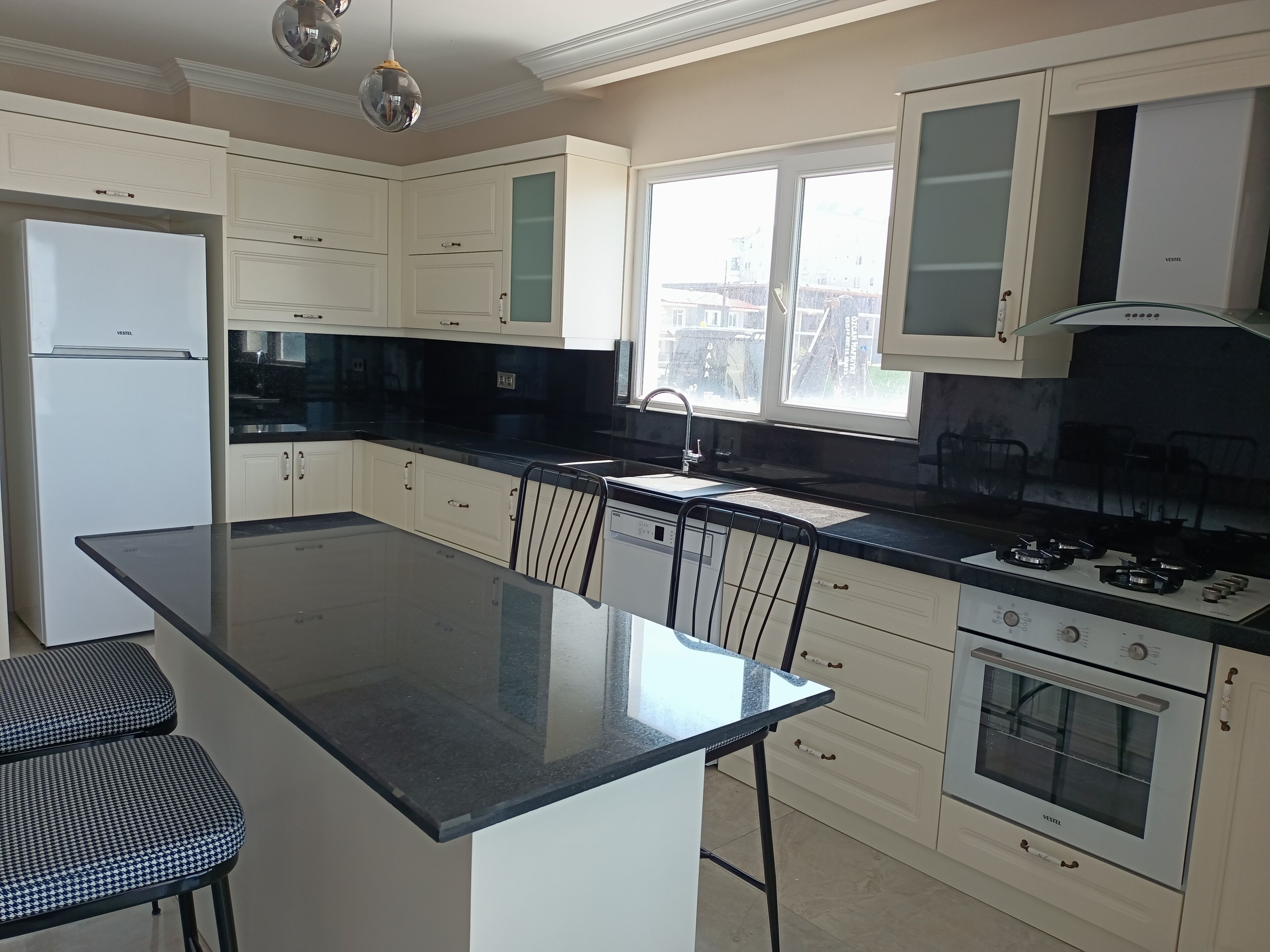 A modern kitchen with a central island, built-in appliances, and a view through the window.