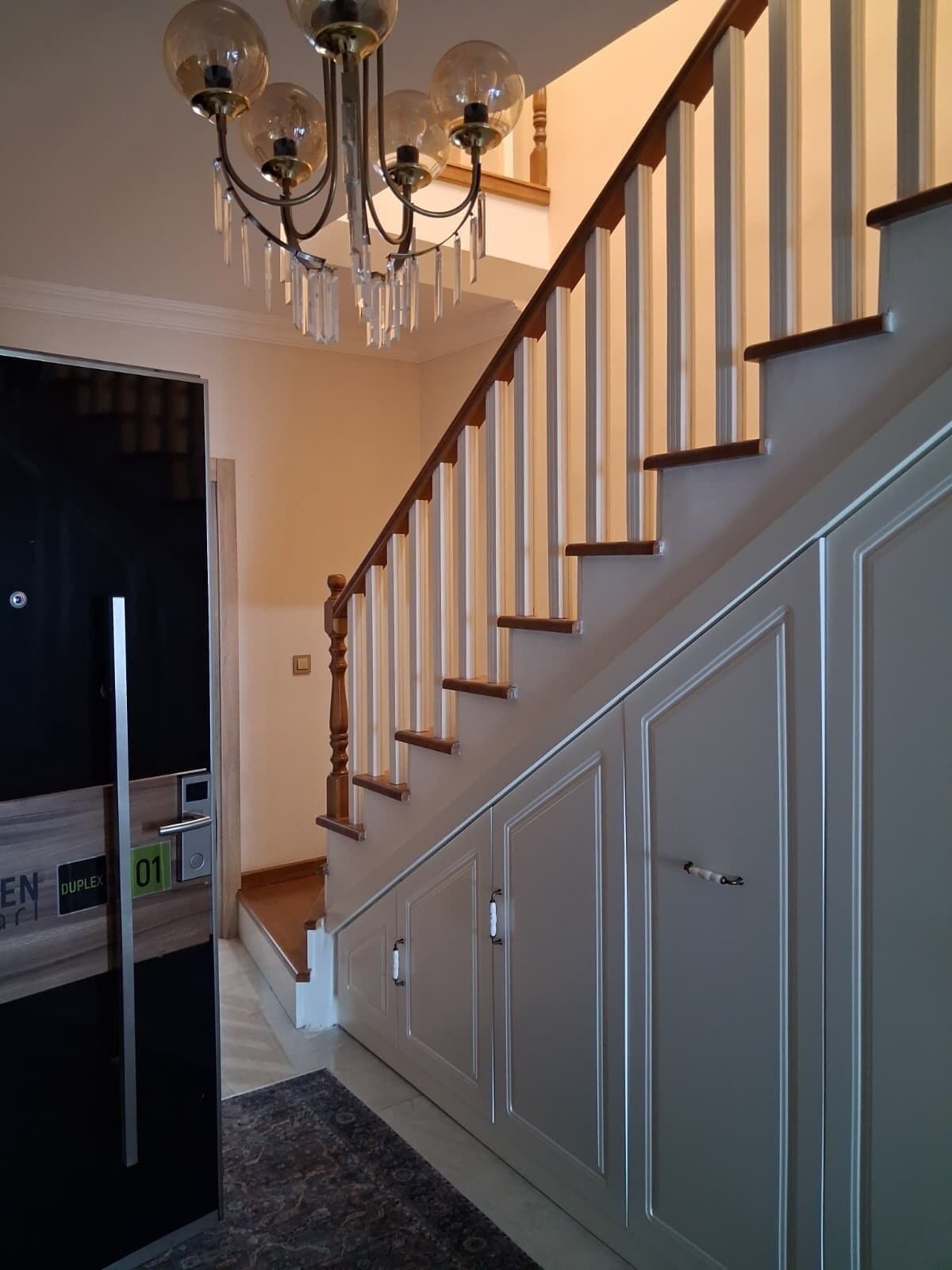 A staircase with wooden steps and a glass railing, leading to a landing with a door.