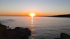 Un capvespre sobre un mar tranquil amb una costa rocosa.