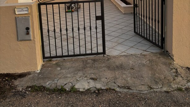 Un pati tancat per una reixa amb un paviment de rajoles, i un edifici amb persianes blaves.