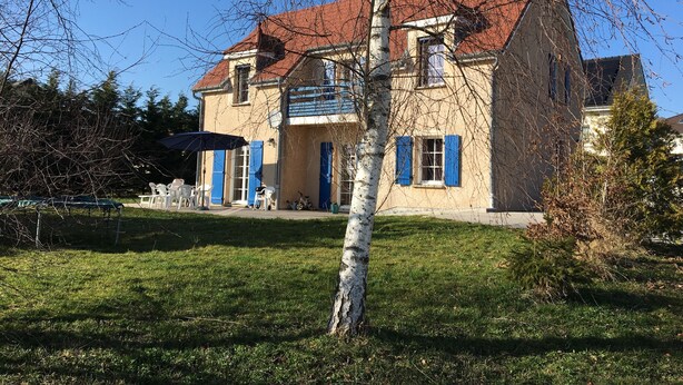 Una casa de dos pisos con techo rojo, contraventanas azules y un pequeño balcón.
