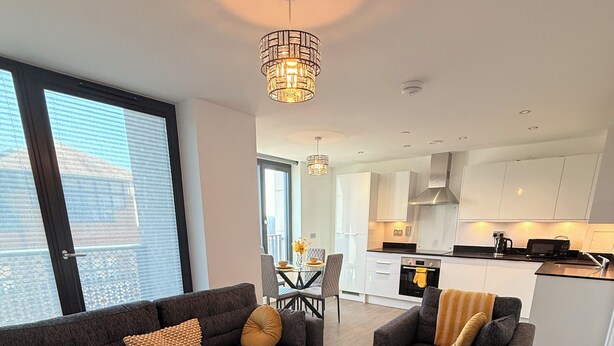 A modern living room with two sofas, a glass coffee table, and a dining area with a table and chairs. - Grace House (St Albans)
