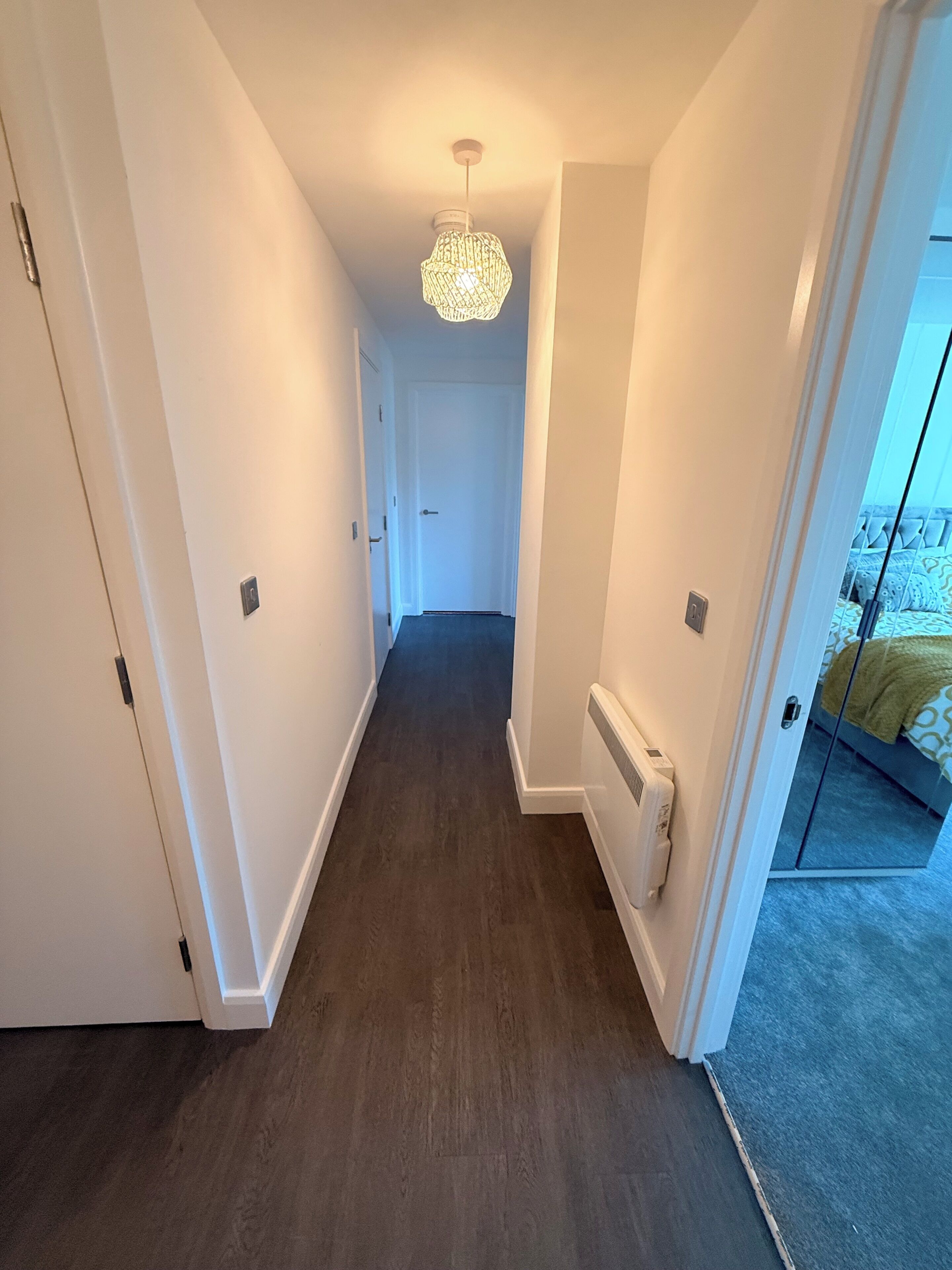 En hall med ett mörkt trägolv, vita väggar och en taklampa.