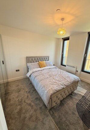 Ein Schlafzimmer mit einer gesteppten Kopfteil, einem Bett mit gemusterten Bettwäsche, einer Pendelleuchte und Blick durch ein Fenster.
