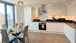 A modern kitchen with white cabinets, a black oven, and a dining area with a glass table and chairs. - Grace House (St Albans)