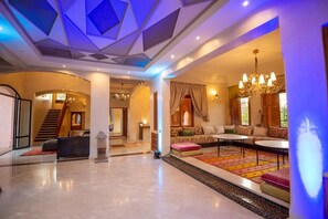 Eine geräumige Lobby mit einer imposanten Treppe, einer Sitzecke mit Sofas und einem Couchtisch sowie einer dekorativen Decke mit geometrischen Mustern.