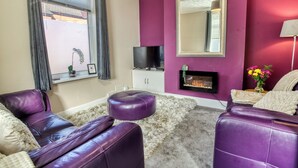 A living room with purple leather sofas, a fireplace, a television, and a large mirror on the wall. - Corner House, close to Lincoln City Centre (Lincoln)